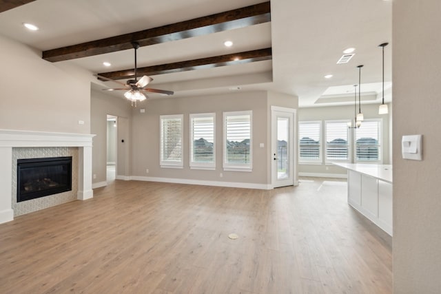 unfurnished living room featuring ceiling fan, beam ceiling, light wood-type flooring, and a tiled fireplace