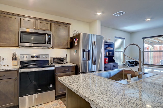 kitchen featuring stainless steel appliances, visible vents, backsplash, a sink, and dark brown cabinetry