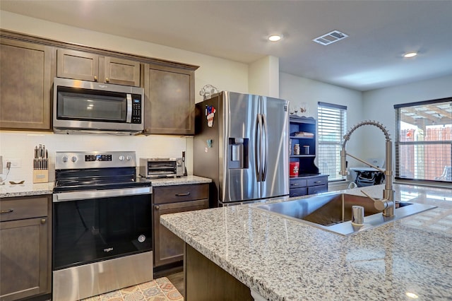 kitchen featuring a sink, backsplash, appliances with stainless steel finishes, visible vents, and dark brown cabinets