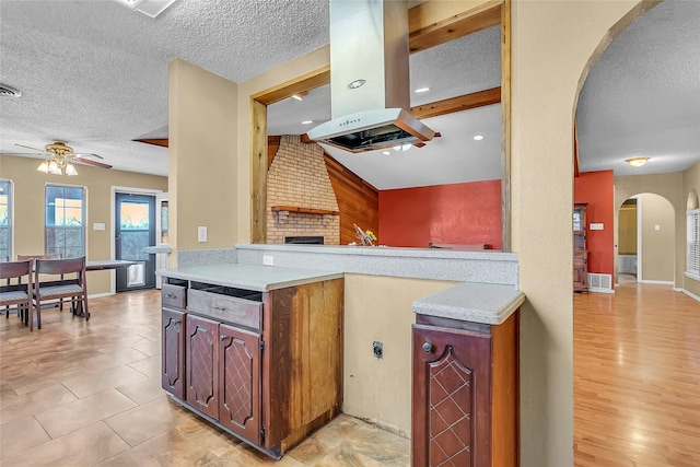 kitchen featuring ceiling fan, a textured ceiling, island exhaust hood, and a fireplace