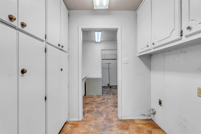 clothes washing area with hookup for an electric dryer, a textured ceiling, and cabinets