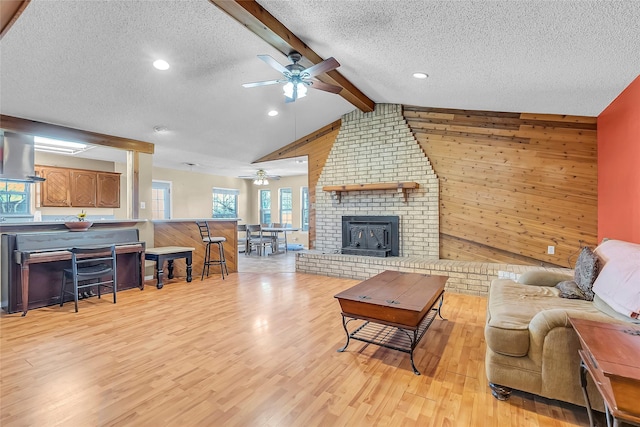 living room featuring wood walls, ceiling fan, light wood-type flooring, a textured ceiling, and lofted ceiling with beams