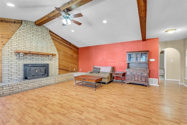 living room featuring light hardwood / wood-style floors, a wood stove, a textured ceiling, and wooden walls