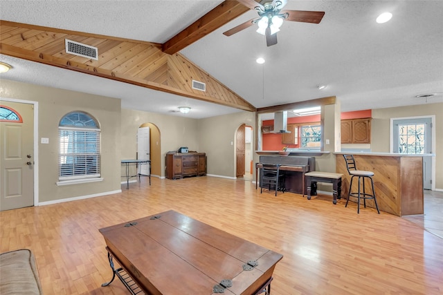 living room with vaulted ceiling with beams, a wealth of natural light, and light hardwood / wood-style floors