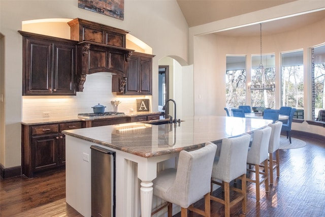 kitchen with light stone countertops, decorative light fixtures, an island with sink, decorative backsplash, and sink