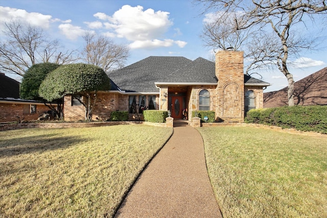 view of front facade with a front yard, brick siding, a chimney, and a shingled roof