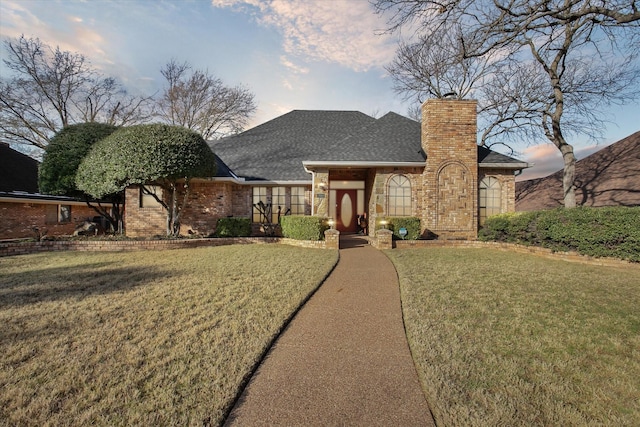 view of front of property featuring a chimney, brick siding, roof with shingles, and a front lawn