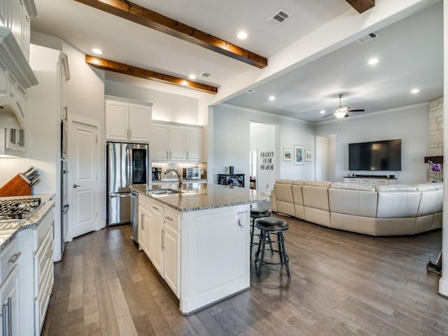 kitchen with a center island with sink, white cabinets, beamed ceiling, and appliances with stainless steel finishes