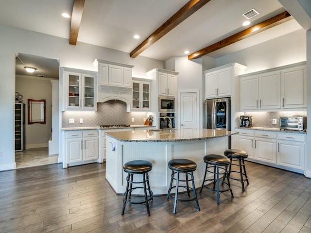 kitchen featuring white cabinetry, stainless steel appliances, beamed ceiling, a kitchen island with sink, and a breakfast bar