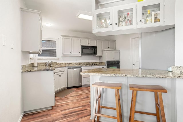 kitchen with black appliances, a kitchen breakfast bar, white cabinets, light stone counters, and kitchen peninsula