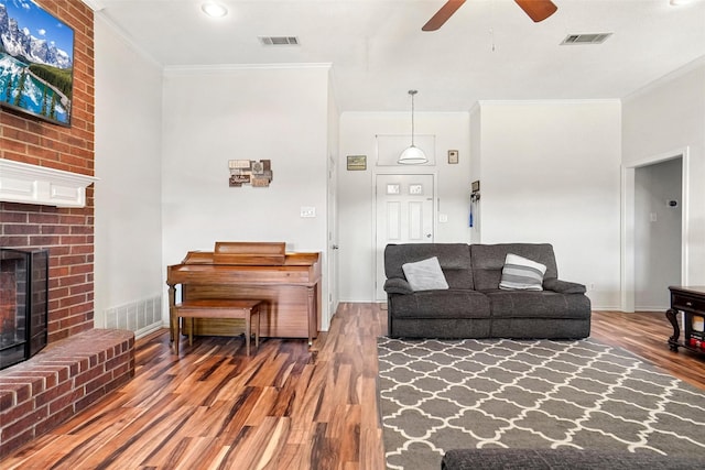 living room with hardwood / wood-style floors, ceiling fan, ornamental molding, and a brick fireplace