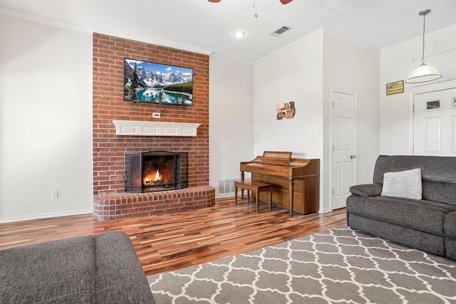 living room featuring hardwood / wood-style floors, a fireplace, ceiling fan, and crown molding