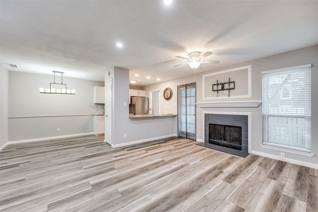 unfurnished living room with light wood-type flooring, ceiling fan, and a tiled fireplace