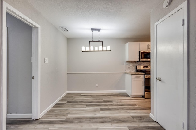 kitchen with appliances with stainless steel finishes, tasteful backsplash, light hardwood / wood-style floors, white cabinetry, and hanging light fixtures