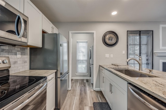 kitchen with light stone countertops, white cabinetry, sink, stainless steel appliances, and backsplash