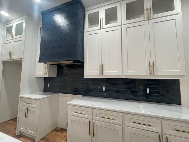 kitchen with light stone countertops, backsplash, premium range hood, and white cabinetry