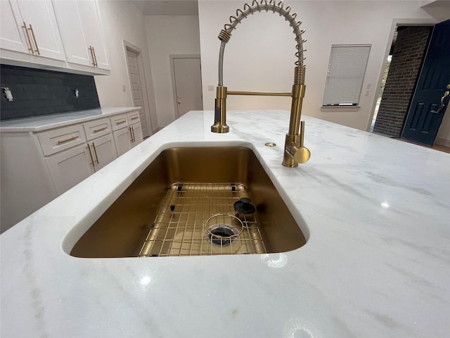 interior details featuring decorative backsplash, white cabinetry, and sink