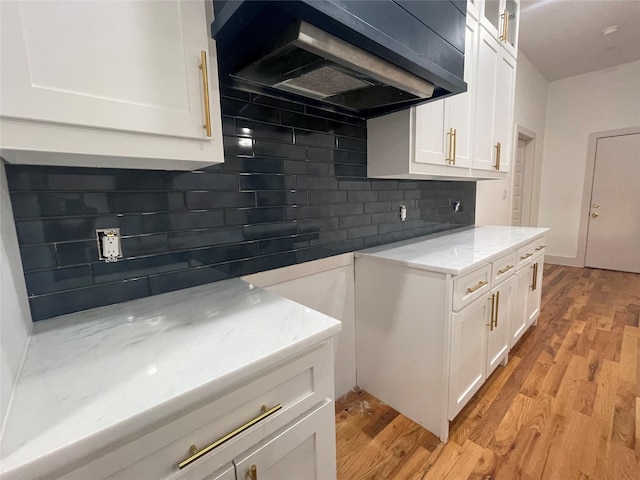 kitchen with white cabinets, light hardwood / wood-style flooring, light stone counters, and wall chimney exhaust hood