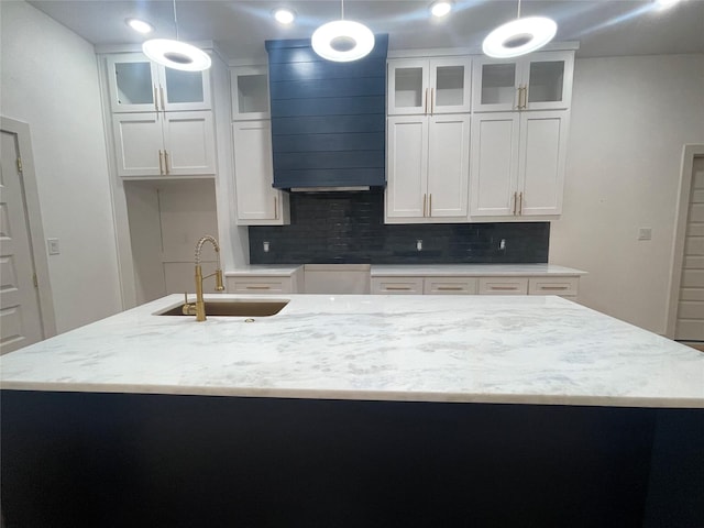 kitchen with white cabinets, pendant lighting, backsplash, and an island with sink