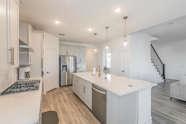 kitchen with sink, hanging light fixtures, stainless steel appliances, backsplash, and a center island with sink