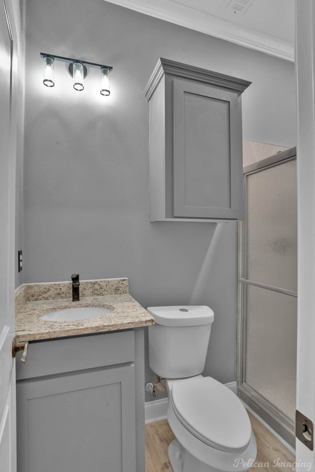 bathroom with hardwood / wood-style floors, toilet, a shower with door, vanity, and ornamental molding