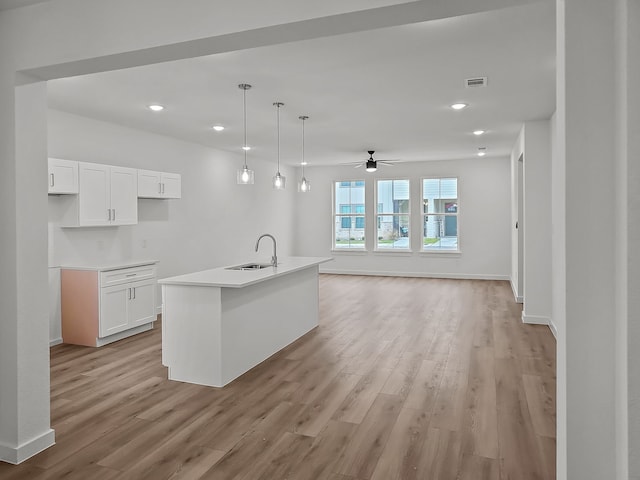 kitchen with decorative light fixtures, white cabinets, a center island with sink, and light hardwood / wood-style floors