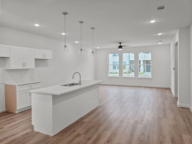 kitchen with sink, white cabinets, ceiling fan, hanging light fixtures, and a kitchen island with sink