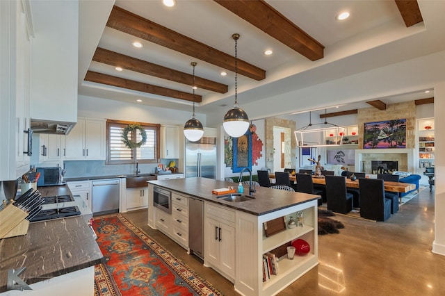 kitchen with sink, built in appliances, hanging light fixtures, a kitchen island with sink, and white cabinets