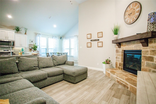 living room featuring a stone fireplace, high vaulted ceiling, and light wood-type flooring