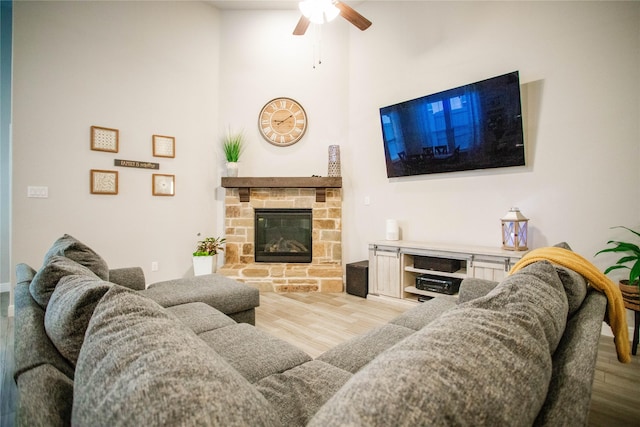 living room with a stone fireplace, ceiling fan, and wood-type flooring