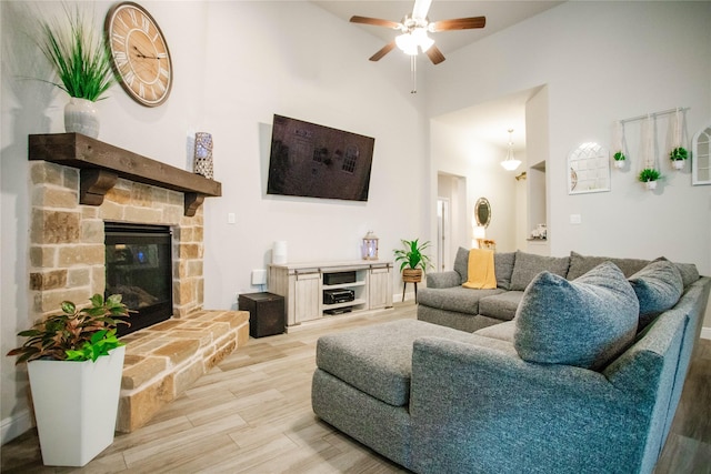 living room with ceiling fan, a stone fireplace, light wood-type flooring, and high vaulted ceiling