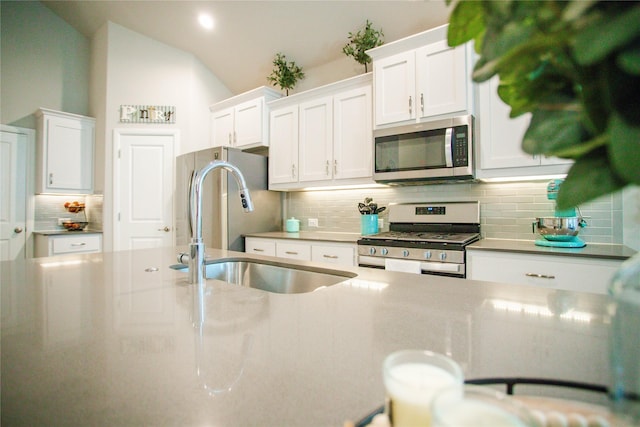 kitchen with white cabinetry, sink, appliances with stainless steel finishes, and vaulted ceiling