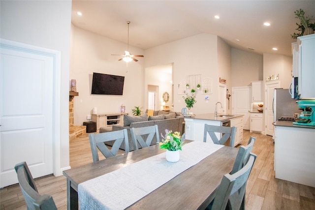 dining space featuring ceiling fan, light wood-type flooring, sink, and high vaulted ceiling