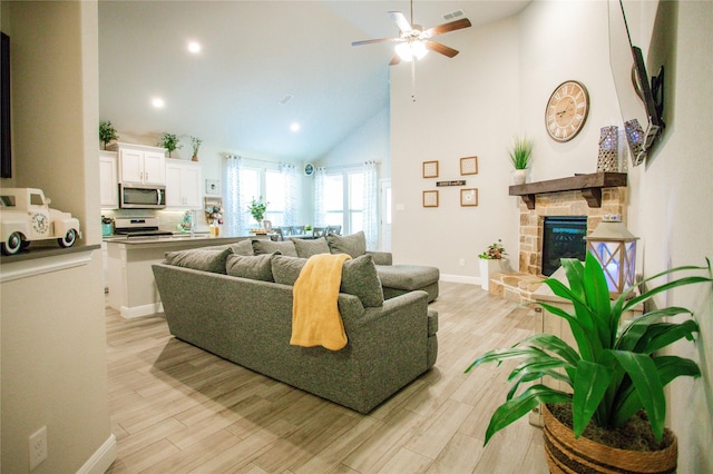 living room with a stone fireplace, ceiling fan, light hardwood / wood-style flooring, and high vaulted ceiling