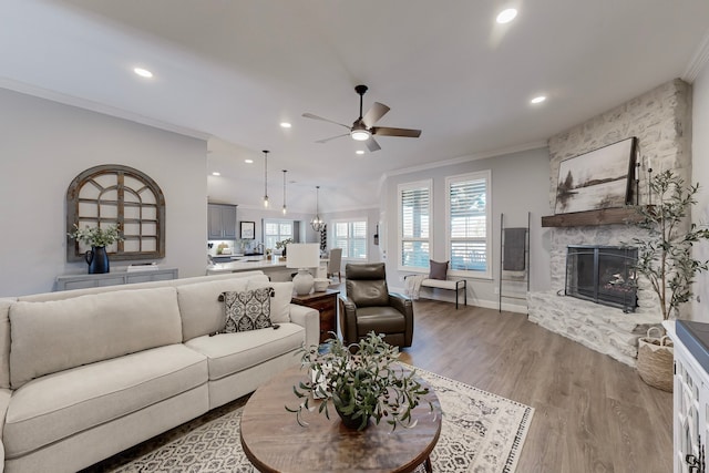 living room with a stone fireplace, ceiling fan, light hardwood / wood-style floors, and ornamental molding