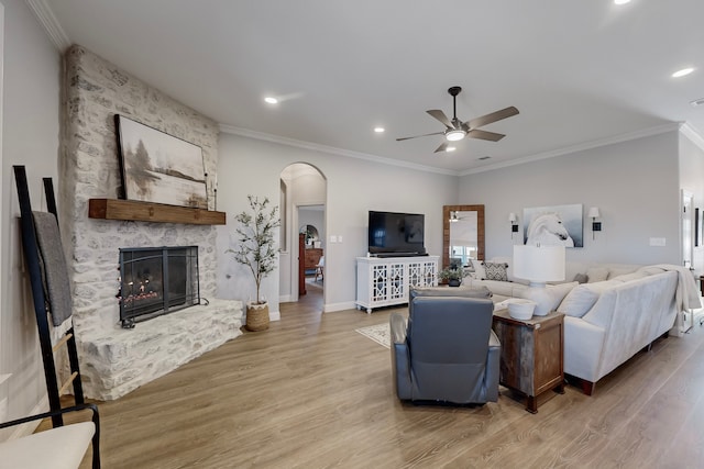 living room with a stone fireplace, ceiling fan, hardwood / wood-style floors, and crown molding