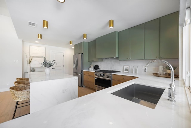 kitchen with wall chimney exhaust hood, green cabinets, stainless steel appliances, a kitchen breakfast bar, and sink