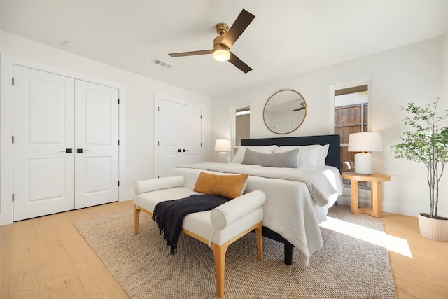 bedroom featuring two closets, ceiling fan, and light hardwood / wood-style floors