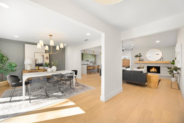 dining area with a brick fireplace, light hardwood / wood-style flooring, an inviting chandelier, and brick wall