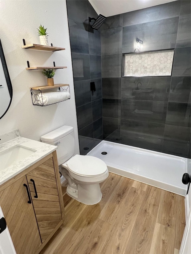 bathroom with toilet, vanity, hardwood / wood-style flooring, and tiled shower