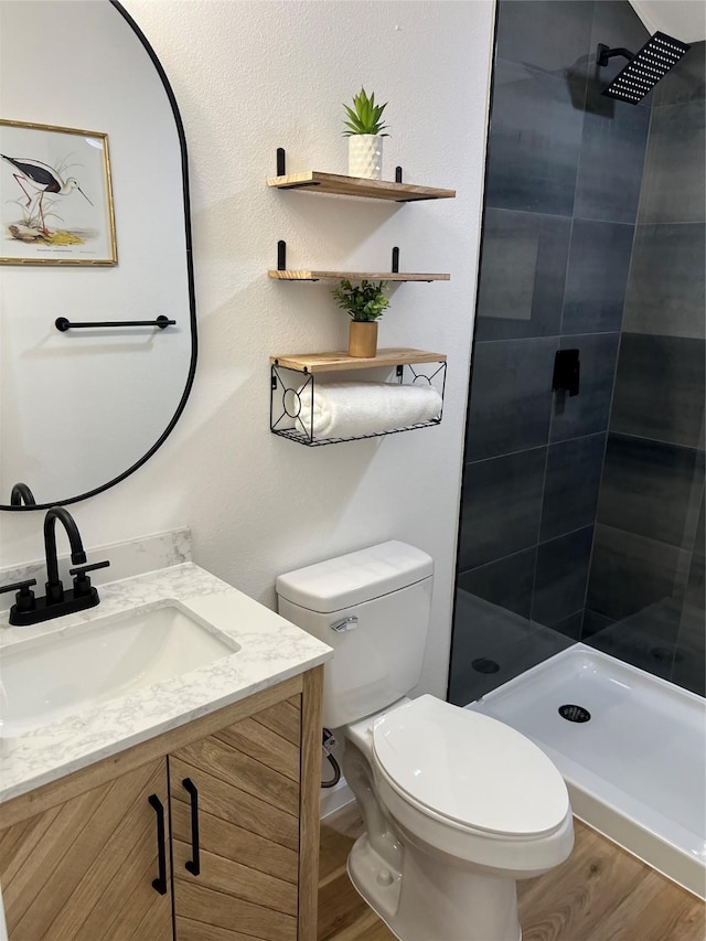 bathroom with toilet, a tile shower, vanity, and hardwood / wood-style floors