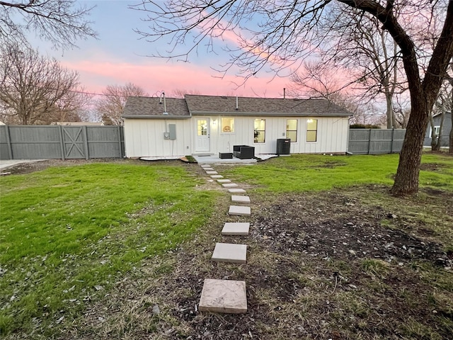 back house at dusk with central AC and a lawn