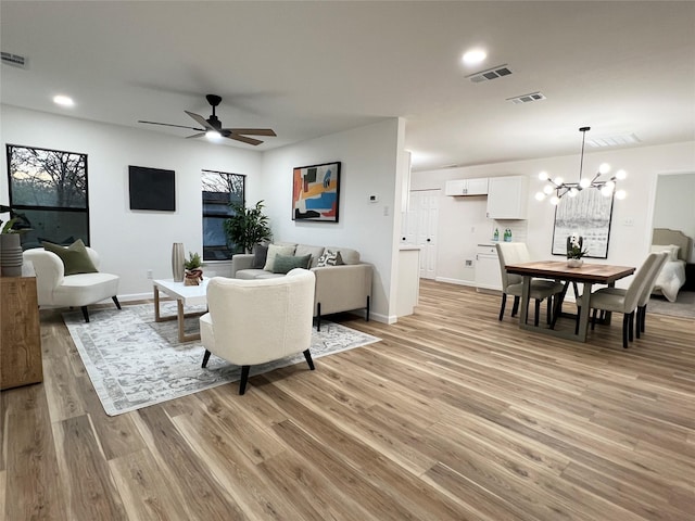 living room with ceiling fan with notable chandelier and light wood-type flooring