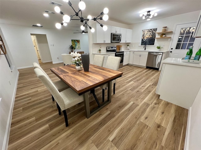 dining room with ceiling fan with notable chandelier, light hardwood / wood-style floors, and sink