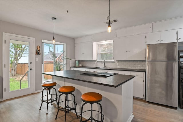 kitchen featuring a center island, white cabinetry, stainless steel refrigerator, and hanging light fixtures