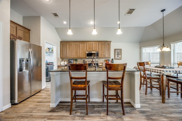 kitchen with light hardwood / wood-style flooring, dark stone counters, an island with sink, stainless steel appliances, and backsplash