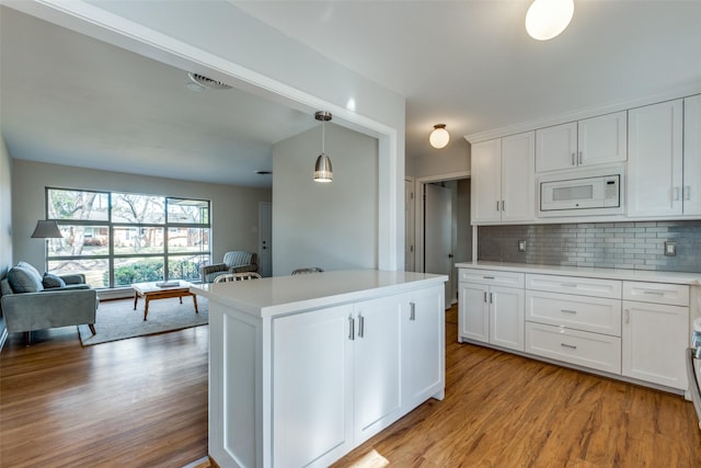 kitchen featuring white microwave, white cabinets, backsplash, and decorative light fixtures