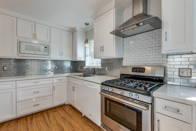 kitchen with tasteful backsplash, white appliances, wall chimney exhaust hood, white cabinets, and sink