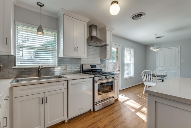 kitchen featuring white cabinetry, stainless steel range with gas stovetop, white dishwasher, wall chimney range hood, and sink