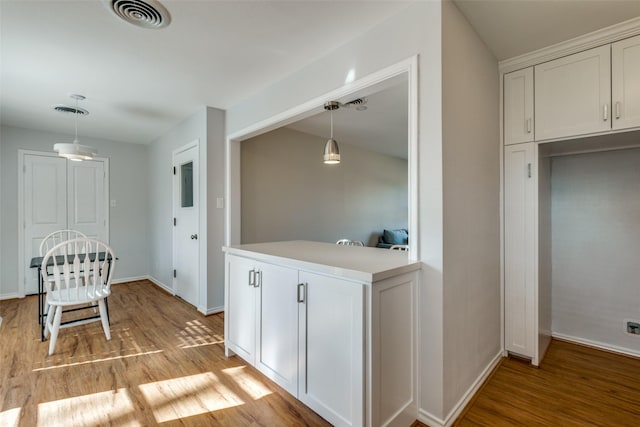 kitchen with kitchen peninsula, light wood-type flooring, white cabinetry, and pendant lighting